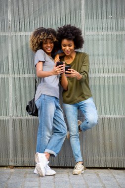 Tam vücut portresi. Cep telefonuyla gülümseyen iki siyah kadın. 