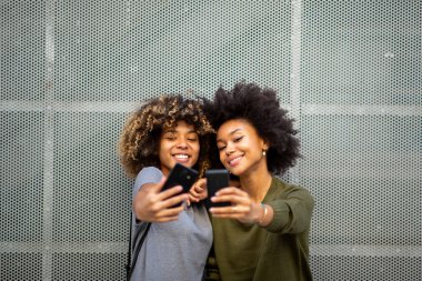 İki mutlu siyahi kadının portresi cep telefonuyla selfie çekiyor. 