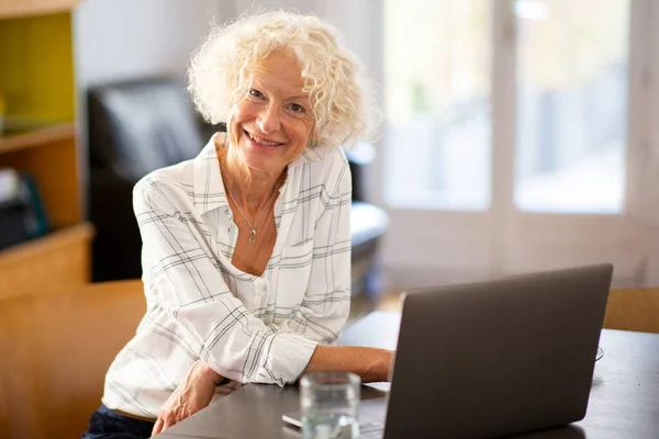 Portrait elderly woman smiling with laptop computer at table
