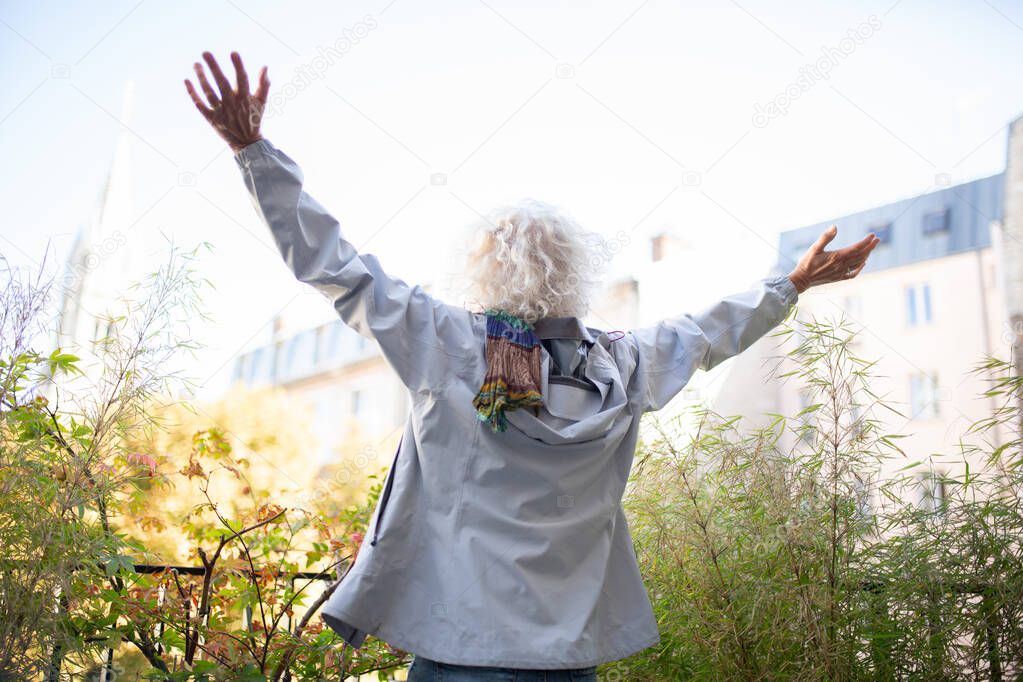 Portrait from behind old woman with arms spread open outside