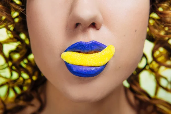 在照片的一部分 女孩的脸 口红蓝色的嘴唇 嘴里的糖是黄色的 黄色背景 免版税图库照片