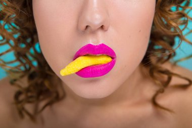 Renkli ruj dudakları ile güzel kız. Kızın ağzına bir sarı şeker var. Kız duygu gösterir.