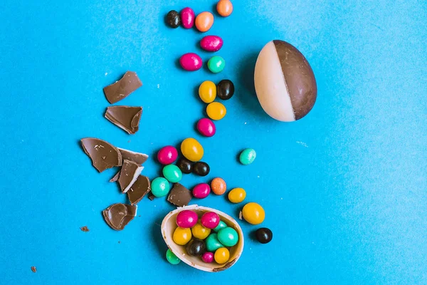 Easter composition with chocolate eggs made of white and black chocolate and dragees of orange, pink, green pieces of chocolate on a colored blue background, place for text