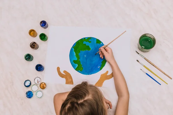 Dünya günü mavi yuvarlak top şeklinde boyanmış avuç içleri bir çocuğun elleri. fırçalar, suluboya, çocuk çizimleri, gouache. Coğrafya gezegeni, küresel felaket.