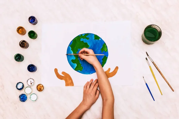 Dünya günü mavi yuvarlak top şeklinde boyanmış avuç içleri bir çocuğun elleri. fırçalar, suluboya, çocuk çizimleri, gouache. Coğrafya gezegeni, küresel felaket.