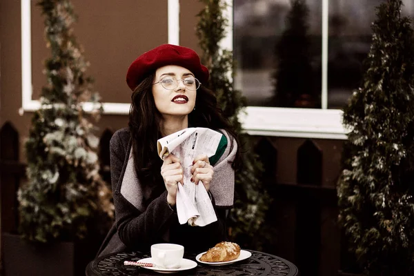 Masada oturan ve kruvasanla kahve içen bir kız..