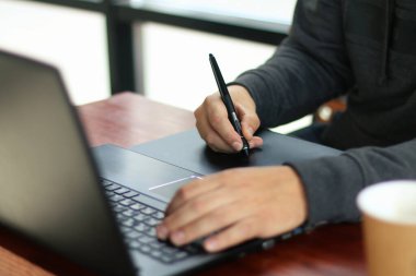 Tasarımcı bir kafede dizüstü bilgisayarla grafik tablet üzerinde çalışıyor