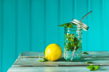 Limonata, soda, limon ve nane yaprakları turkuaz arka planda kavanozda..