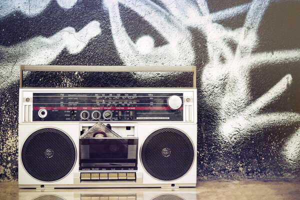 Old boom box with cassette on the floor and on a graffiti background. Remembering the music of yesterday.