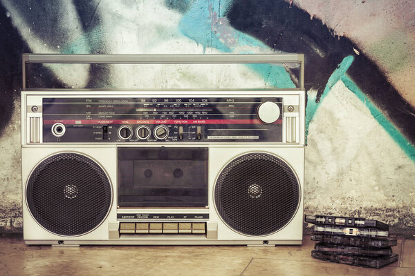 Vintage ghetto blaster with plenty of musical cassettes on grungy background with graffiti. Remembering and listening to music from the past.