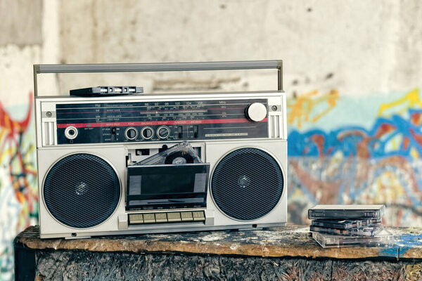 Vintage ghetto blaster with plenty of musical cassettes on grungy background with graffiti.