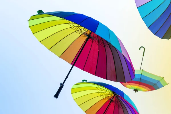 Open umbrellas with bright colors of the rainbow fly on yellow-blue pastel background. Umbrellas flying in the sky with the colors of Pride Day. LGBT party.