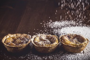 Belem 'den zanaatkar hamur işleri, Portekiz' den geleneksel tatlı. Ev yapımı lezzetli Belem kekleri. Koyu renkli ahşap bir masanın üzerine krema serpiştirilmiş. Kremalı pasta..