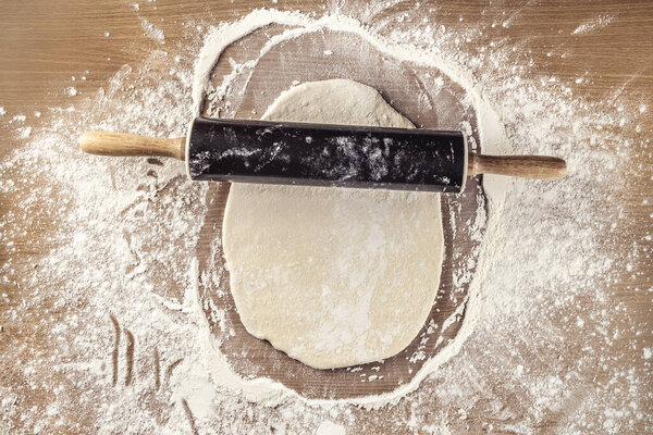 Сырое тесто, которое смешивают с кухонным роликом на очень мучном деревянном столе. Изображение сверху. Приготовление пищи, свежая еда готова к приготовлению. Фотография еды
.