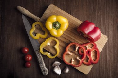 Kiraz domatesleri, sarımsak ve biberler kırsal bir masada mutfak tahtasındaki eski bir bıçakla kesilmiş. Doğal ürünler. Sağlıklı yiyecekler. Doğa ve refah..