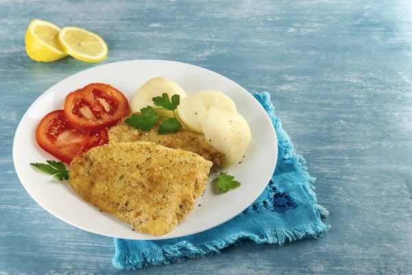 Taze maydanoz ve limonla tatlandırılmış ve yanında pişirilmiş patates ve domates ile birlikte sağlıklı pişmiş bir balığın yakın çekimi. Mavi arka plan. Sağlıklı beslenme için besleyici gıda kavramı.