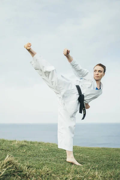 Young female redhead karate athlete hitting a high kick