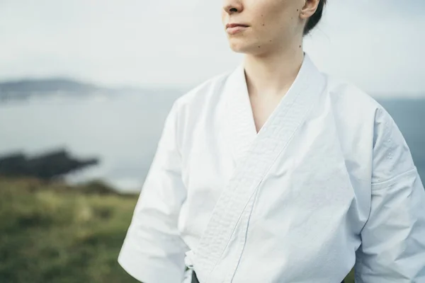 Unknown young female karate athlete looking away on top of a cliff