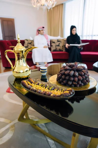 An Arab family in traditional dress eats dates and drinks tea in the holy month of Ramadan on Iftar. Feast in honor of Eid Mubarak. The family sits on a background of plates with dates, dried fruits