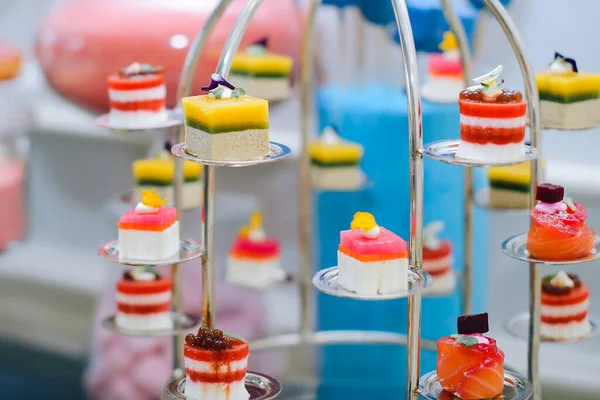 Unusual table setting made of desserts in a metal construction made in bright colors. Cakes made from different fillings and decorated with berries
