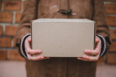 Elinde basit bir karton paket taşıyan kahverengi ceketli bir adam.