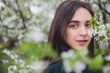 Beyaz tişörtlü, siyah saçlı, yeşil ceketli, güzel beyaz kiraz ağacının yanında yaşayan beyaz tenli bir kız.