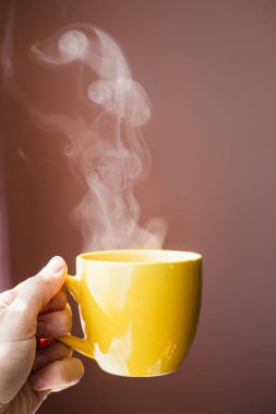 Sarı fincanlı sıcak çay elinde koyu pembe arka planda güzel bir sabah ışığı olan bir içecek.