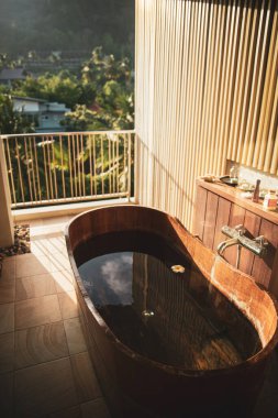 Kahverengi ahşap küvet, balkonda suyla dolu. Tayland 'ın başkenti Krabi' deki Ao Nang köyünde yeşil ormanlar ve palmiye ağaçları manzaralı.