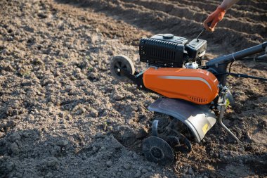 small orange plowing machine in hands of a farmer making arable in black soil clipart