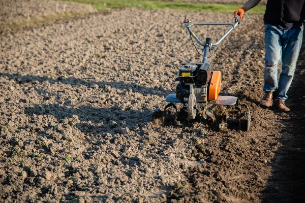 黒い土で耕す農家の手にある小さなオレンジの耕作機 — ストック写真