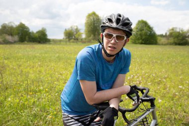 Bisikletli, kasklı, yeşil tişörtlü, yeşil yaz tarlasında bisiklet süren, doğa koşullarında etkin, sağlıklı yaşam tarzı olan bir adam.