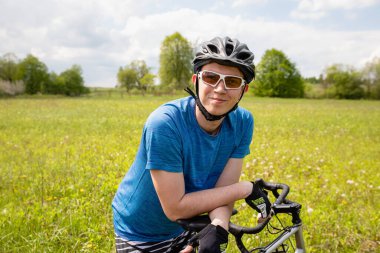 Bisikletli, kasklı, yeşil tişörtlü, yeşil yaz tarlasında bisiklet süren, doğa koşullarında etkin, sağlıklı yaşam tarzı olan bir adam.