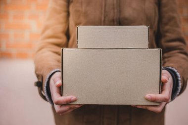 Kahverengi ceketli adam elinde teslimattan kalma iki tane karton paket tutuyor.