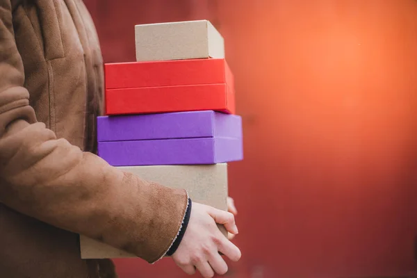 Person in brown coat holding four colorful paper carboard delivery package with red background