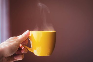 Sarı fincanda sıcak çay elinde koyu pembe arka planda güzel bir sabah ışığı olan içecek.