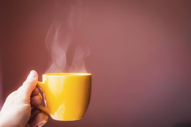 Sarı fincanda sıcak çay elinde koyu pembe arka planda güzel bir sabah ışığı olan içecek.