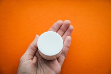 Beyaz krema paketi parlak turuncu arka planda, güzellik ürünüyle yüzleş