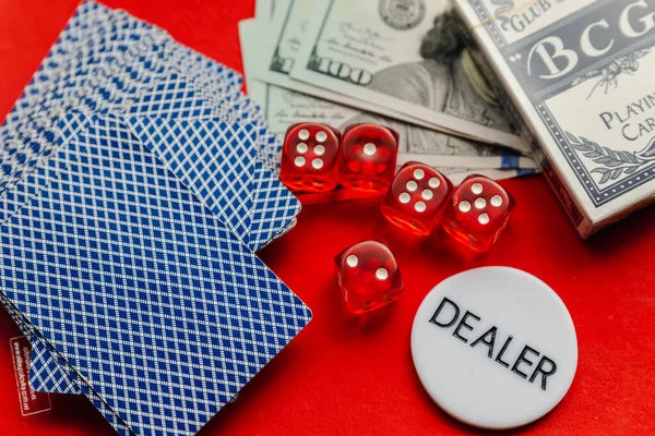 Poker cards, red dices and stack of dollars with white dealer sign on red background