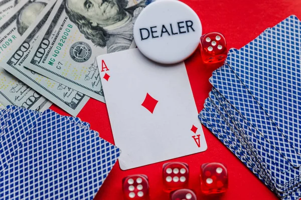 Poker cards, red dices and stack of dollars with white dealer sign on red background