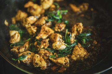 Tayland fesleğeni kızartma tavasında kontrol ediliyor, geleneksel kızartılmış yemek pişiriliyor, yeşil fesleğen yaprağıyla doğranmış tavuk pirzolası kızartılıyor.