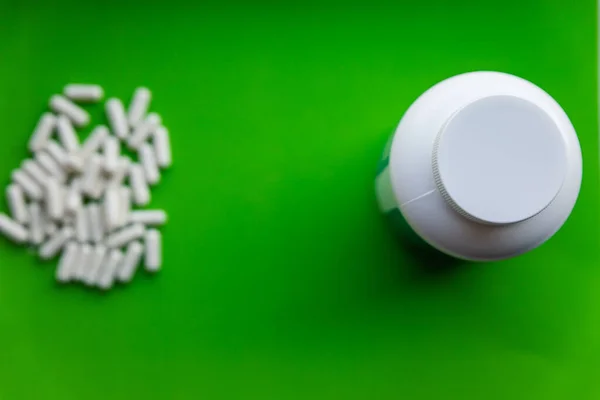 White bottles of vitamin supplements with empty white cap on bright green background with heap of white pills