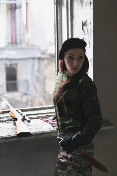 Девушка в военной форме с огнестрельным оружием в заброшенном здании. Девушка в зеленой камуфляжной одежде у окна с винтовкой . — стоковое фото