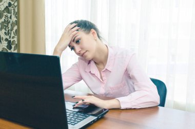 Bilgisayarın başında başını tutan çok yorgun bir kız..