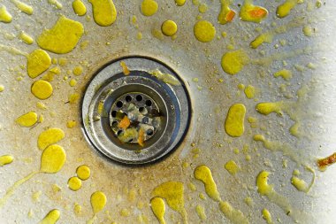 A dirty and littered sink with yellow grease stains.