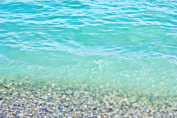 Close-up-of-a-soft-turquesa-wave-and-coastal-pebbles-under-transparent-sea-water — Fotografia de Stock