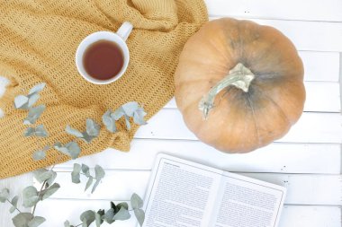 Sarı yorganın üzerinde gri bir fincan kahve ve beyaz ahşap zeminde balkabağı romantik bir sonbahar iç mekanı.