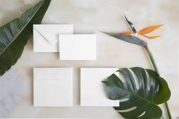 Lege kaart met envelop op marmeren tafel en tropische bloemen. Mockup sjabloon met bovenaanzicht. Strelitzia bloemen en monstera bladeren op marmeren vloer — Stockfoto