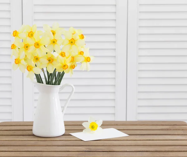 Κεφαλές λουλουδιών Daffodil σε καφέ ξύλινο τραπέζι λευκό πρόσκληση κάρτα tempate και λευκά παντζούρια στο παρασκήνιο — Φωτογραφία Αρχείου