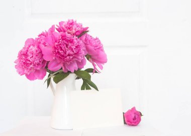 Beyaz emaye vazoda pembe şakayıklar. İç tasarımda çok güzel çiçekler var. Davetiye metni için beyaz kağıt, vazoda beyaz şakayıklar, iç dekorasyon