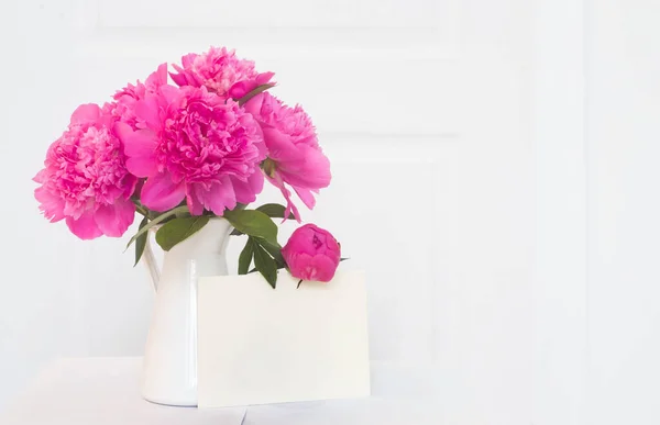 Pedónias cor-de-rosa em vaso esmaltado branco. Lindas flores em design de interiores. Livro branco para texto de convite, peônias brancas em um vaso, decoração de interiores — Fotografia de Stock